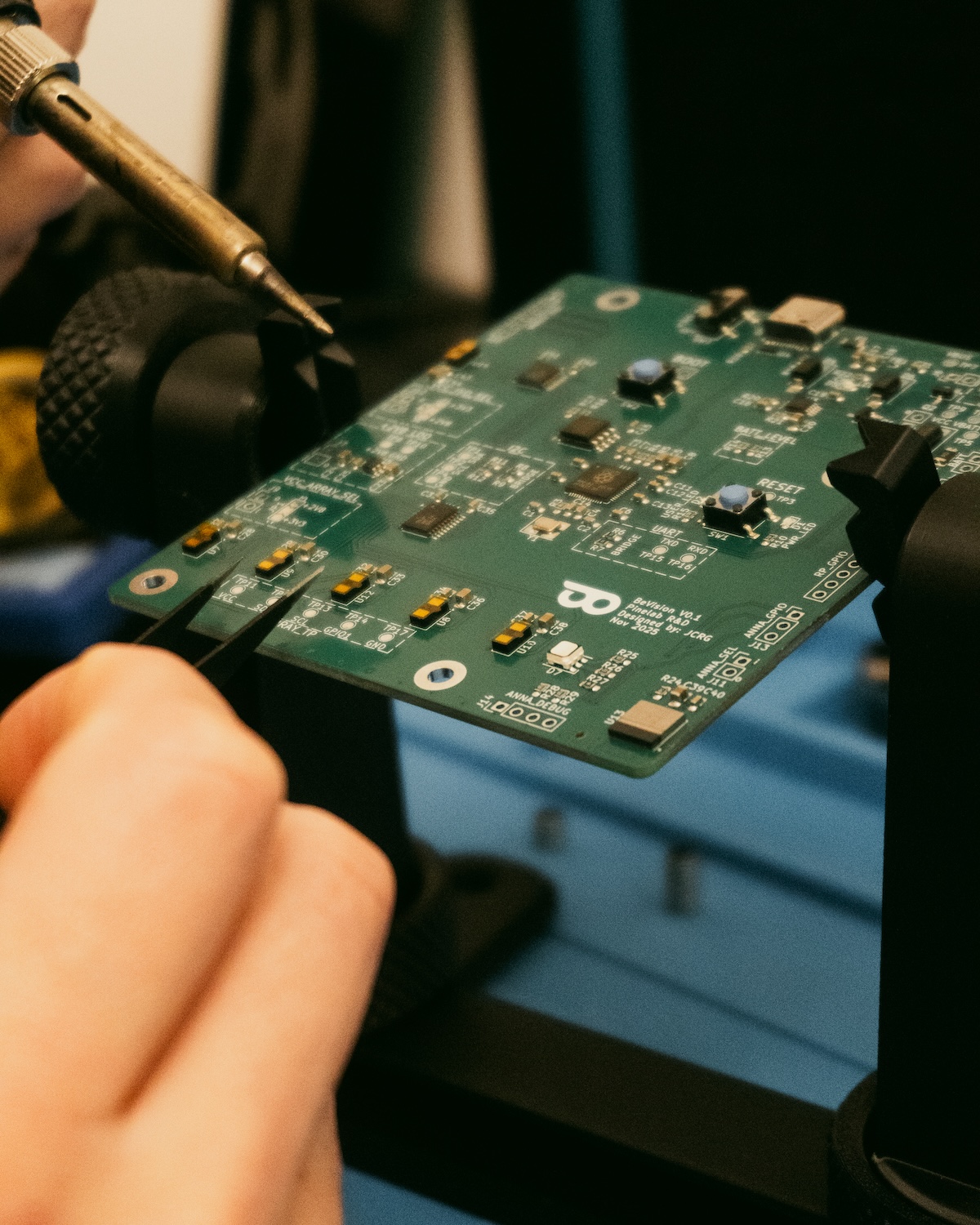 Hands working on PCB assembly with soldering iron and tweezers